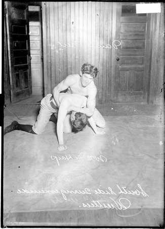 Wrestlers, South Side Turngemeinde, William Harp and Dan O'Neil, O'Neil is holding Harp by the armpit, kneeling in a room - Chicago Daily News, Inc.