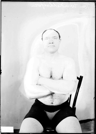 Wrestler Tom Winkelfoefer, sitting in front of a light-colored backdrop in a room - Chicago Daily News, Inc.