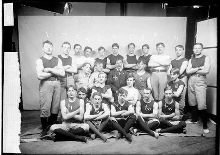 Northwestern Turner Schaft wrestlers and instructor Frederick L. Jahn (wearing a suit) posing in front of a light-colored backdrop - Chicago Daily News, Inc.