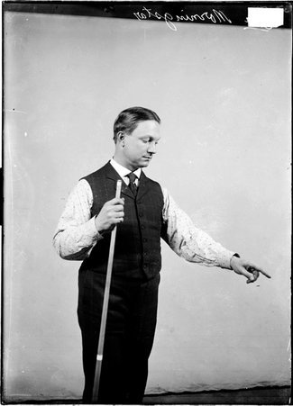 Billiards player, Ora Morningstar, holding pool cue and pointing in front of a light colored backdrop in a room - Chicago Daily News, Inc.