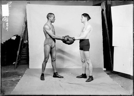 Boxer, Joe Gans, shaking hands with unidentified boxer, both men wearing boxing gloves, in a room - Chicago Daily News, Inc.
