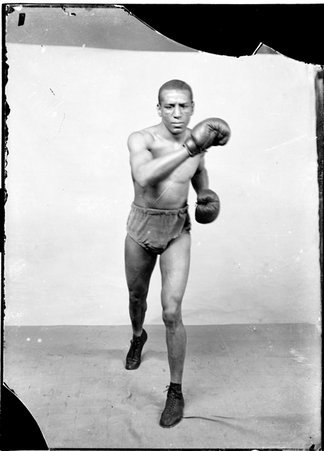 Boxer, Joe Gans, in boxing stance with right arm extending across his chest in a room - Chicago Daily News, Inc.