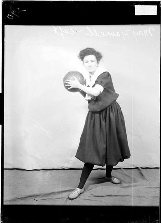 Basketball player , May Howell, holding a basketball, standing in front of a light-colored backdrop - Chicago Daily News, Inc.