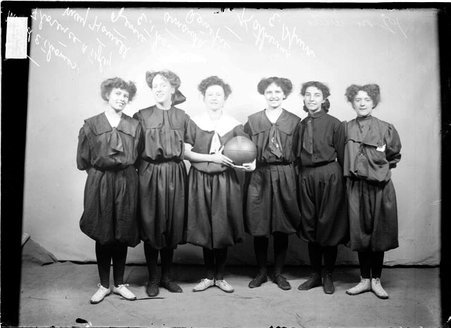 Basketball players, May Howell, Katherine, Florence Tyley, Maud Thomas, Jessie Thomas, and Amanda Renspie standing by a backdrop - Chicago Daily News, Inc.