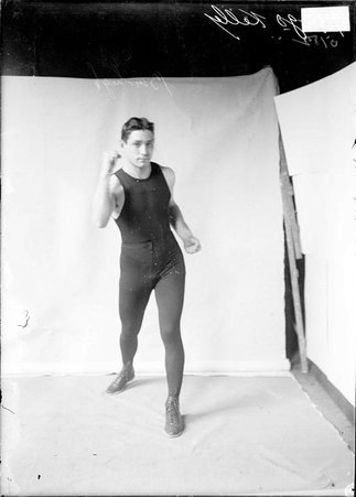 Boxer, Hugo Kelly, standing in boxing stance with right fist at chin level in a room - Chicago Daily News, Inc.