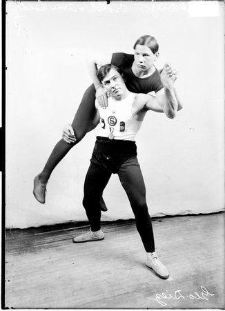 Wrestlers, George Diez performing a crotch and shoulder maneuver on Emil Diez, standing in front of a backdrop, text on image - Chicago Daily News, Inc.