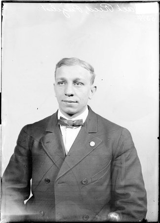 Pugilist, Jack Reed, wearing a suit, sitting in front of a light-colored backdrop in a room - Chicago Daily News, Inc.