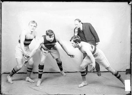 Basketball players, Mac Bear, Garrison, Snow, and Levey, in blocking positions while an official looks on in front of a backdrop - Chicago Daily News, Inc.