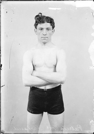 Pugilist Patrick McFarland, standing in front of a light-colored backdrop in a room - Chicago Daily News, Inc.