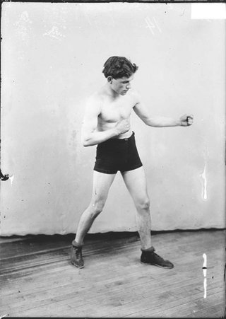 Pugilist Patrick McFarland, standing in profile in a boxing stance in front of a light-colored backdrop in a room - Chicago Daily News, Inc.