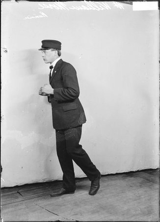 Runner William Morse, wearing a suit and hat, standing in profile in front of a light-colored backdrop in a room - Chicago Daily News, Inc.