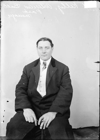 Artesians baseball manager Ed Kelly wearing a suit, sitting in front of a light-colored backdrop in a room - Chicago Daily News, Inc.