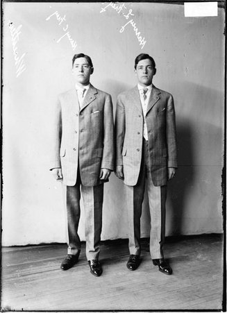 Wrestlers Harry C. Frey and Harvey L. Frey wearing suits, standing in front of a light-colored backdrop in a room - Chicago Daily News, Inc.