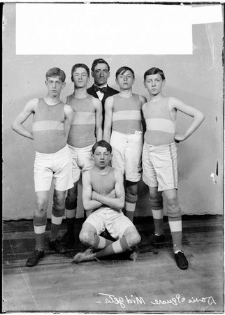 Davis Square midgets basketball players, and a man wearing a suit posing in front of a light-colored backdrop in a room - Chicago Daily News, Inc.