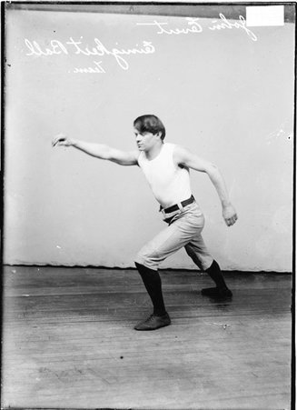 Einigkeit indoor baseball player John Evert, leaning forward, extending his right arm in front of him, standing in front of a backdrop - Chicago Daily News, Inc.