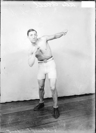 Pugilist Abe Attell, throwing a left hook, standing in a boxing stance in front of a light-colored backdrop in a room - Chicago Daily News, Inc.