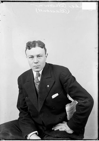 Baseball player Jake Brown, wearing a suit with a folded newspaper in his jacket pocket, sitting in front of a backdrop, dark exposure - Chicago Daily News, Inc.