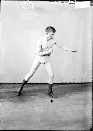 Pugilist Battling Nelson, leaning forward and extending his left arm, standing in a boxing stance in front of a backdrop - Chicago Daily News, Inc.