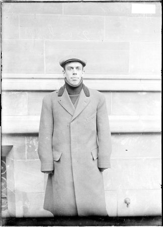 University of Chicago athlete Merriam, wearing a cap and overcoat, standing in front of a building on the University of Chicago campus - Chicago Daily News, Inc.