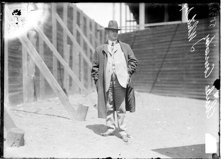 Chicago White Sox president Charles Comiskey, standing behind wooden wall supported by wooden beams at South Side Park, light exposure - Chicago Daily News, Inc.