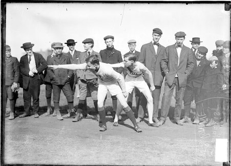 Runners Crane and Morris, leaning forward and extending their right arms back, as if taking part in a relay race, at Marshall Field - Chicago Daily News, Inc.