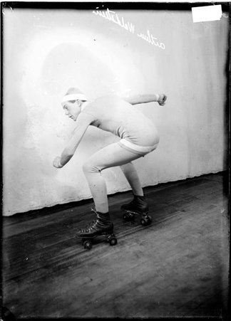 Roller skater Arthur Waldstein, wearing roller skates and tights, crouching in front of a light-colored backdrop - Chicago Daily News, Inc.
