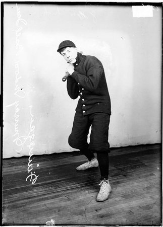Murray indoor baseball player Finnegan, holding a bat over his right shoulder standing in front of a light colored background in a room - Chicago Daily News, Inc.
