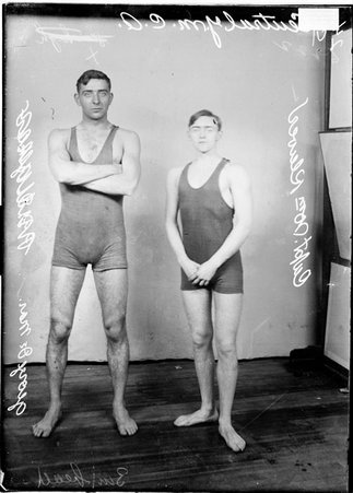 Central YMCA swim team captain, William Klewer, and water polo team captain, George De Mar, standing in front of a backdrop - Chicago Daily News, Inc.