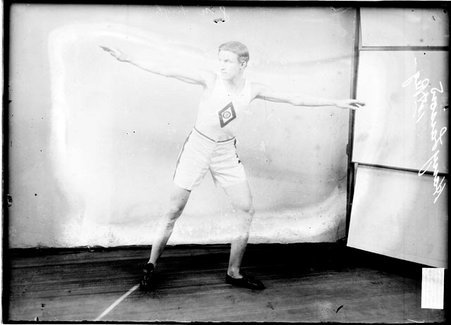 Runner, Harry Larson, standing in a room with his arms straight out to his sides - Chicago Daily News, Inc.
