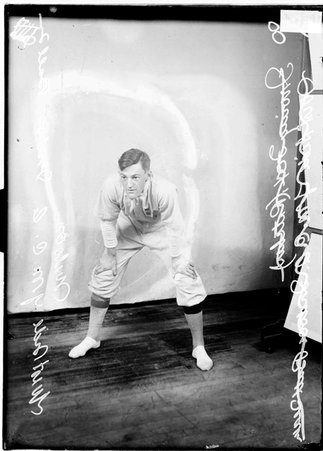 Indoor baseball player, West Side, YMCA, leaning forward, hands on his knees, standing in front of a backdrop - Chicago Daily News, Inc.