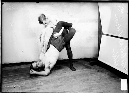 Illinois Athletic Club wrestlers Robert Sargisson and Louis Houston, performing a maneuver in front of a backdrop in a room - Chicago Daily News, Inc.