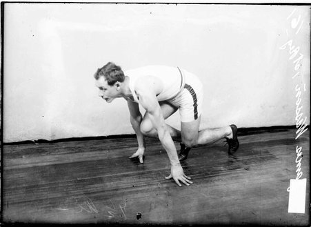 Athlete, James Wasson, crouching on the floor as if starting a race in a room - Chicago Daily News, Inc.