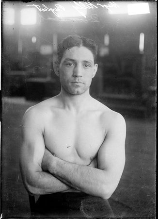 Boxer Hugo Kelly, standing with his arms crossed on his chest in a room - Chicago Daily News, Inc.
