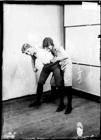 Wrestlers, John Nemec holding C. Papse in a choker hold in front of a light colored background in a room - Chicago Daily News, Inc.