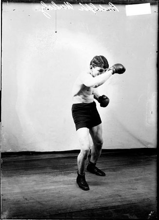 Boxer Rudolph Unholz, blocking with his right arm in front of his face standing in front of a backdrop - Chicago Daily News, Inc.