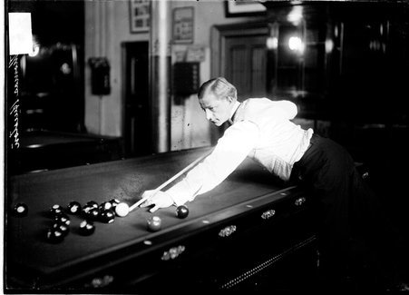 Billiards player Thomas Hueston, aiming a cue at cue ball, with his left side to the camera in a room - Chicago Daily News, Inc.