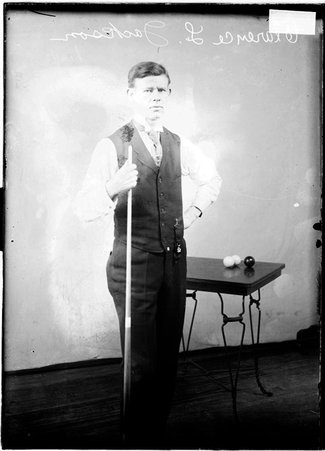 Billiards player Clarence Jackson, holding cue, standing in front of three balls sitting on a table - Chicago Daily News, Inc.
