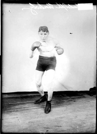 Boxer Rudolph Unholz, with his knees bent and fist ready standing in front of a backdrop - Chicago Daily News, Inc.