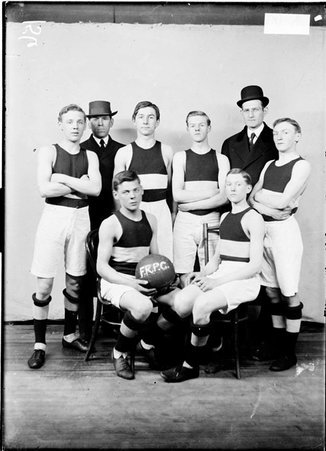 Unidentified basketball team and coaches posing in front of a light colored background in a room - Chicago Daily News, Inc.