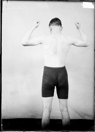 Pugilist, Packey McFarland, standing in a room with his back to the camera flexing his biceps and back muscles - Chicago Daily News, Inc.