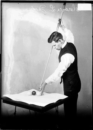 Billiards player Clarence Jackson, holding cue vertically, aiming at cue ball next to two others sitting on a table - Chicago Daily News, Inc.