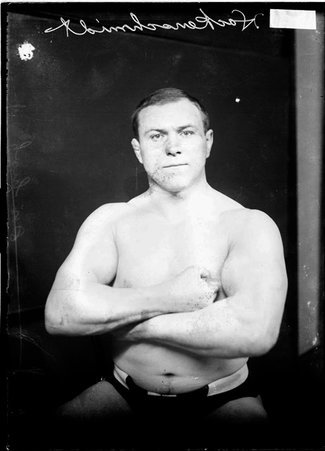 Wrestler George Hackenschmidt, standing with his arms crossed on his chest in front of a backdrop - Chicago Daily News, Inc.