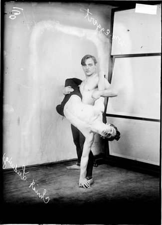 Wrestlers, Eggert is standing in a room holding Ludwig's leg and arm across his body - Chicago Daily News, Inc.