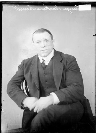 Wrestler, George Hackenschmidt, sitting in a chair in front of a light backdrop, wearing a suit - Chicago Daily News, Inc.