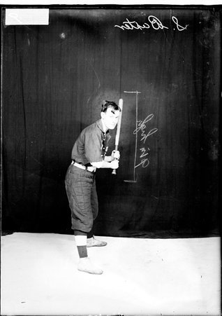 Indoor baseball player S. Baxter, holding a bat, standing in a batting stance in front of a dark backdrop in a room - Chicago Daily News, Inc.