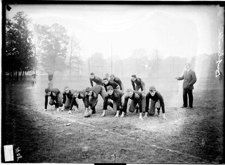 Lake Forest Academy football team facing the camera, crouching in an offensive line formation on an athletic field, light exposure - Chicago Daily News, Inc.