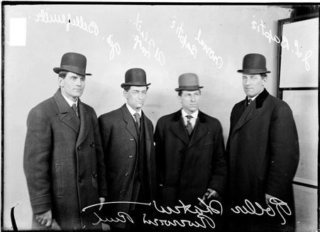 Roller skaters Al Flath, George Bellefenille, Norval Baptie and J. L. Baptie, standing in front of a light colored background in a room - Chicago Daily News, Inc.