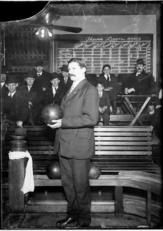 Bowler L. Langmeyer holding a bowling ball, standing in front of a ball-return track in a bowling alley, text reads Phoenix League - Chicago Daily News, Inc.