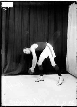 University of Illinois basketball player T. E. Thompson holding a basketball and leaning forward, standing in front of a backdrop - Chicago Daily News, Inc.