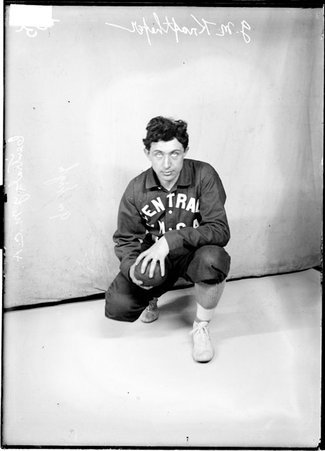 Central YMCA indoor baseball player J. M. Krifthefer, holding a ball, kneeling in front of a light-colored backdrop - Chicago Daily News, Inc.